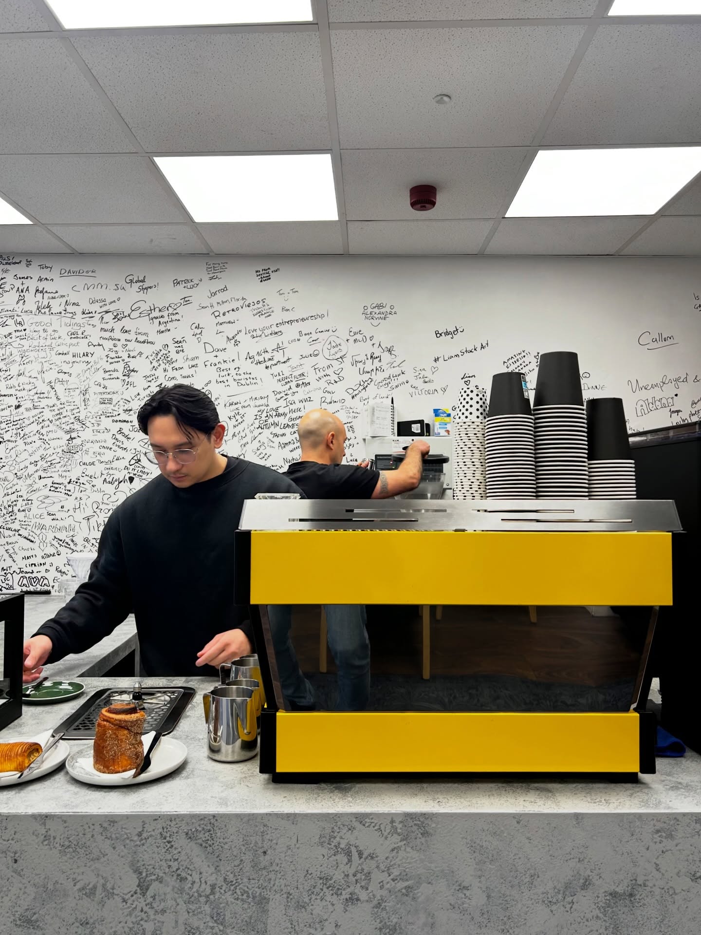 Yellow La Marzocco espresso machine at the bar, signature wall behind